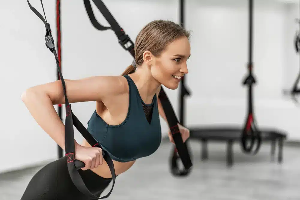 mujer entrenando brazos con correas de fitness trx